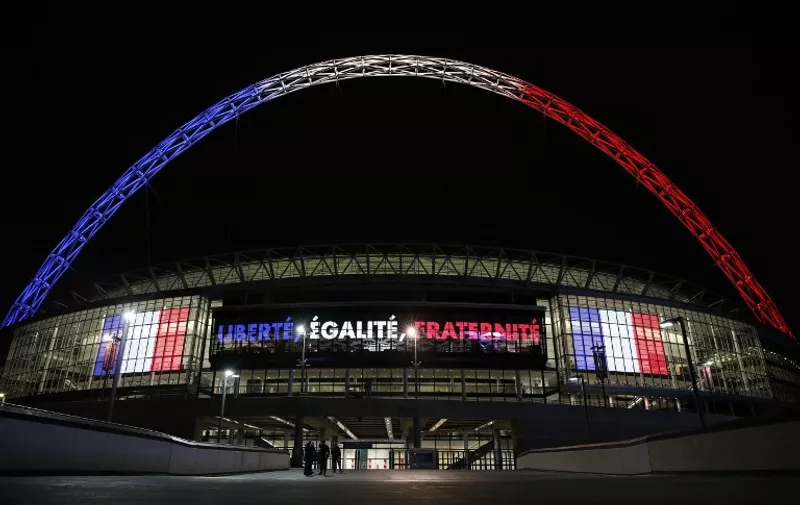 The arch of London's Wembley Stadium is illuminated with the colours of the French national flag with French flags flanking the Liberte, Egalite, Fraternite moto of France  in west London on November 16, 2015, as Britons express their solidarity following a spate of coordinated attacks in Paris on November 13 that left at least 129 people dead. Armed police will be deployed around London's Wembley Stadium at an international friendly between England and France on November 17 as part of increased security measures following the Paris attacks, a senior officer said.  AFP PHOTO / ADRIAN DENNIS
