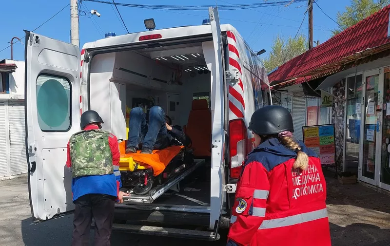 A wounded man is carried into an ambulance by medics at a market in the center of the Ukrainian city of Kherson following a Russian shelling, on April 18, 2023. - After Putin's visit was made public on Tuesday, Ukrainian officials said Russian forces had shelled the center of Kherson, killing one and injuring nine. (Photo by Dina Pletenchuk / AFP)