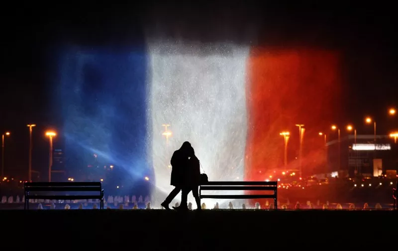 A young couple stands in front of illuminated waters with the colors of the French national flag on November 16, 2015 to pay tribute to victims of the attacks claimed by Islamic State which killed at least 129 people and left more than 350 injured on November 13. AFP PHOTO / STRINGER