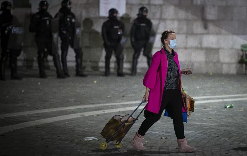 A woman with a shopping trolley walks past police officers wearing anti-riot gear as protesters clash with police during the rally against governments coronavirus restrictions in Ljubljana on November 5, 2020. (Photo by Jure Makovec / AFP)