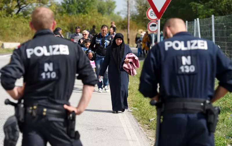 Austrian policemen watch as migrants cross the Hungarian-Austrian near Nickelsdorf, eastern Austria, on September 10, 2015. Austrian Railways on Thursday suspended services to Hungary as it struggled to cope with thousands of migrants arriving from over the border after travelling up through the Balkans. Hungary's border with Serbia has become a major crossing point into the European Union.  AFP PHOTO / JOE KLAMAR