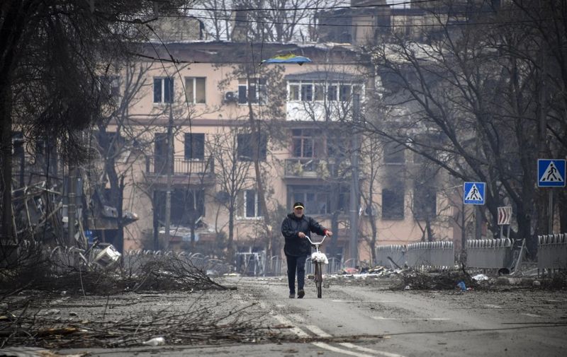 A man walks with a bicycle in downtown Mariupol on April 12, 2022, as Russian troops intensify a campaign to take the strategic port city, part of an anticipated massive onslaught across eastern Ukraine, while Russia's President makes a defiant case for the war on Russia's neighbour. - *EDITOR'S NOTE: This picture was taken during a trip organized by the Russian military.* (Photo by Alexander NEMENOV / AFP)