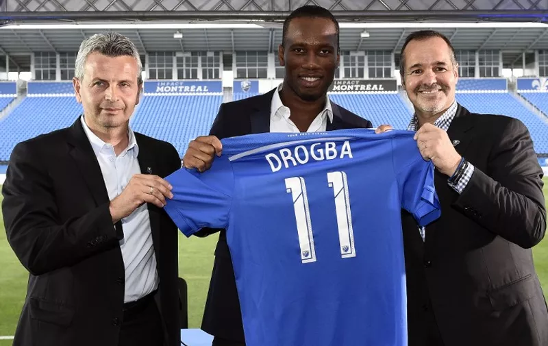 Ivorian striker Didier Drogba (C) poses with a jersey between Montreal president Joey Saputo (R) and head coach Franck Klopas on July 30, 2015 in Montreal. Former Chelsea star Didier Drogba joined Major League Soccer's Montreal Impact on July 27, 2015, the Ivory Coast striker signing with the Canadian club after a rights transfer from the Chicago Fire. AFP PHOTO/FRANCK FIFE
