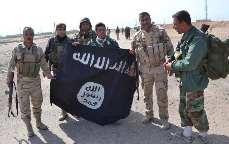 Iraqi Kurdish Peshmerga fighters pose for a photo holding an Islamic State (IS) group flag in the village of Sultan Mari west of the city of Kirkuk on March 9, 2015 after they reportedly re-took the area from IS jihadists. IS spearheaded a sweeping offensive in June 2014 that overran large parts of the country north and west of Baghdad, including in Kirkuk province. AFP PHOTO / MARWAN IBRAHIM