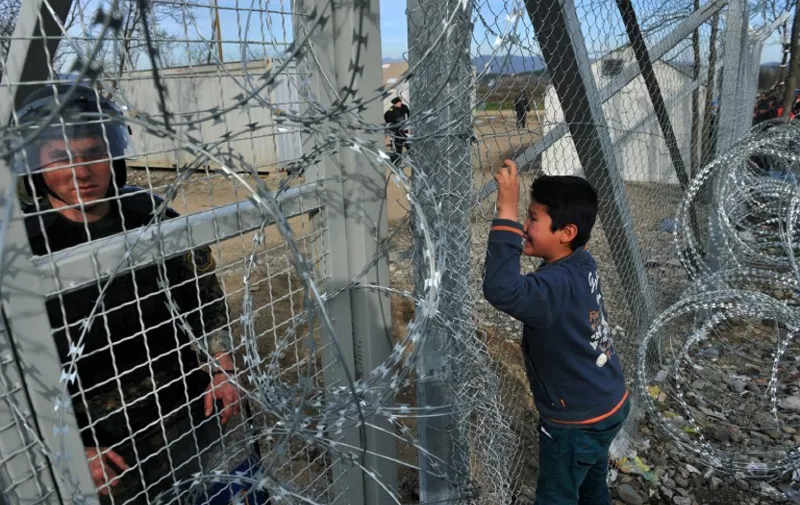 A Macedonian police officer looks on as young boy from Afghanistan cries and places his face against the fence at the Greece-Macedonia border during a demonstration near the village of Idomeni, northern Greece, on February 22, 2016, against Macedonia's refusal to allow Afghans to pass the border. 
Greece said on February 22 that it was taking action to persuade Macedonia to take in Afghan migrants as thousands remained stranded at the border and the main port in Athens. About 5,000 refugees and migrants are stuck at the border with Macedonia after the neighbouring non-EU state on February 21 refused to allow passage to Afghans, police said. / AFP / SAKIS MITROLIDIS
