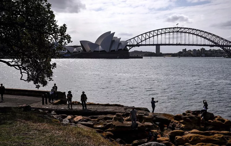 Tourists stand on rocks as they take photographs in front of the Sydney Opera House and Sydney Harbour Bridge on a spring day on November 13, 2023. (Photo by DAVID GRAY / AFP)