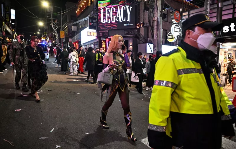 EDITORS NOTE: Graphic content / A policeman walks past revellers in the neighbourhood of Itaewon in Seoul on October 30, 2022, near to the location where a Halloween stampede took place. - More than 140 people were killed on October 29 and some 150 were injured in a horrific stampede in central Seoul when a large crowd celebrating Halloween crammed into a narrow street, officials said. (Photo by Anthony WALLACE / AFP)