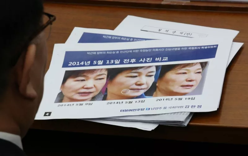 Kim Young-jae, who heads a hospital which was regularly visited by South Korea's impeached President Park Geun-hye's longtime confidante Choi Soon-Sil, looks at a combination of pictures of Park during a hearing at the National Assembly in Seoul on December 14, 2016. 
The text on the poster reads "The photos are comparing Park's face around May 13th". South Korea's embattled president was visited by "shadowy", unchecked doctors for anti-ageing treatments including injections of human placenta extract, a parliamentary enquiry into a growing corruption scandal heard on December 14. / AFP PHOTO / POOL / AHN Young-Joon