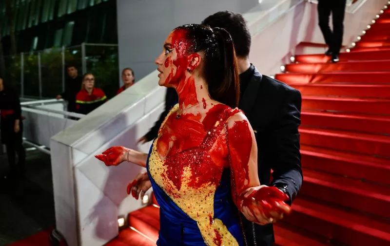 A protester, wearing a dress in the colours of the Ukrainian flag, is detained by security after she covered herself in fake blood on the stairs on the Festival Palace ahead of the screening of the film "Acide" during the 76th edition of the Cannes Film Festival in Cannes, southern France, on May 21, 2023. (Photo by CHRISTOPHE SIMON / AFP)