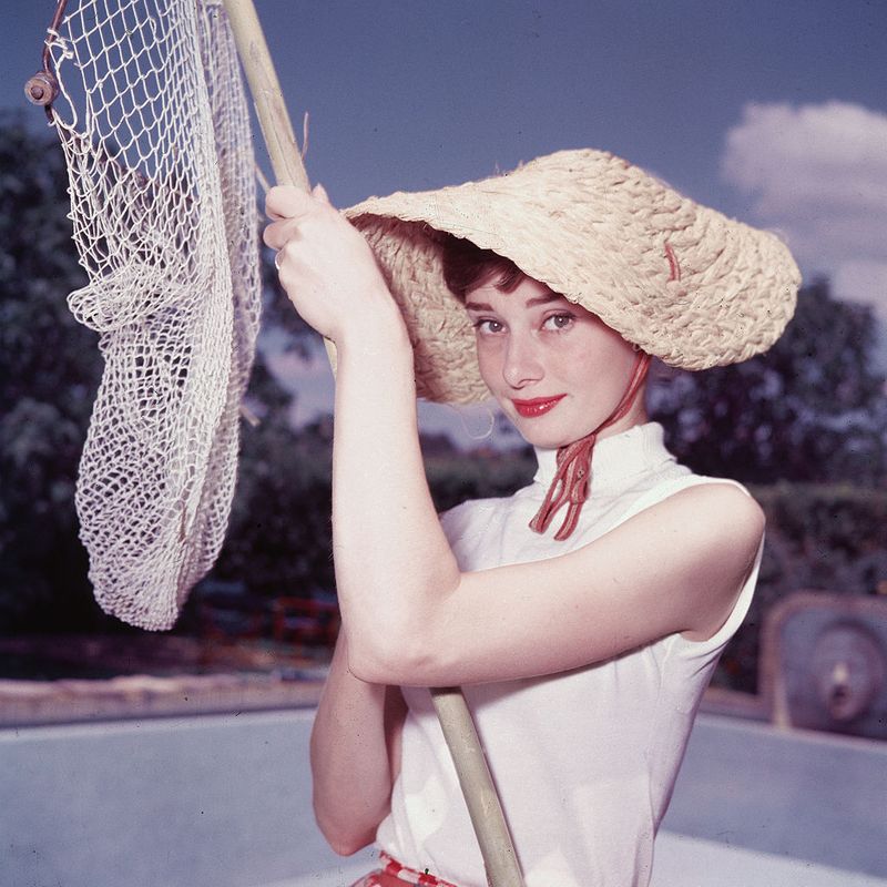 Portrait of Belgian-born American actress Audrey Hepburn (1929 - 1993) as she wears a peculiar hat and sleeveless blouse and holds a pool cleaning net beside a dry swimming pool, early 1950s. (Photo by Hulton Archive/Getty Images)
