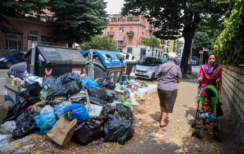 Residents walk past overflowing trash bins on July 10, 2019 in the Centocelle district of Rome, as the Italian capital struggles with a renewed garbage emergency aggravated by the summer heat. (Photo by Tiziana FABI / AFP)