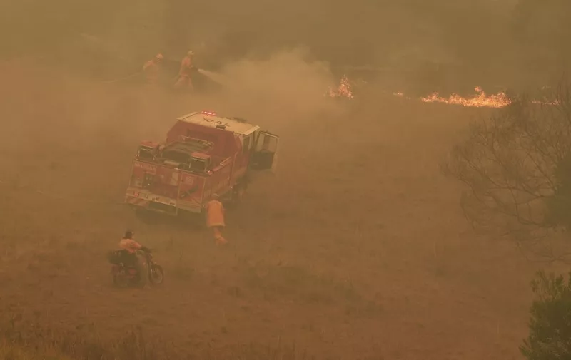 A farmer (bottom) watches as firefighters (top) put out flames near the town of Taree, some 350kms north of Sydney, on November 14, 2019. - The death toll from devastating bushfires in eastern Australia has risen to four after a man's body was discovered in a scorched area of bushland, police said on November 14. (Photo by WILLIAM WEST / AFP)