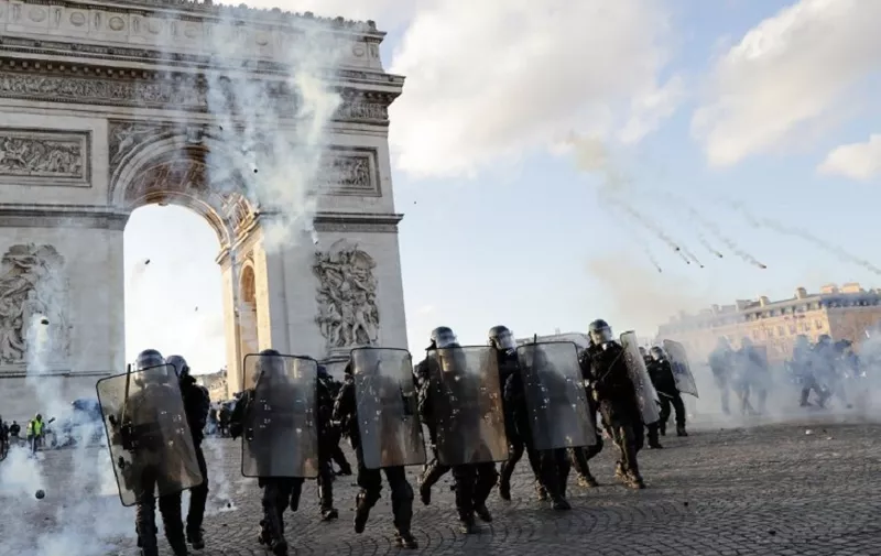Riot police charge using tear gas canister at the Arc de Triomphe on the Place de l'Etoile in Paris on March 16, 2019, during clashes with Yellow Vest protesters, on the 18th consecutive Saturday of demonstrations called by the 'Yellow Vest' (gilets jaunes) movement. - Demonstrators hit French city streets again on March 16, for a 18th consecutive week of nationwide protest against the French President's policies and his top-down style of governing, high cost of living, government tax reforms and for more "social and economic justice." (Photo by Thomas SAMSON / AFP)