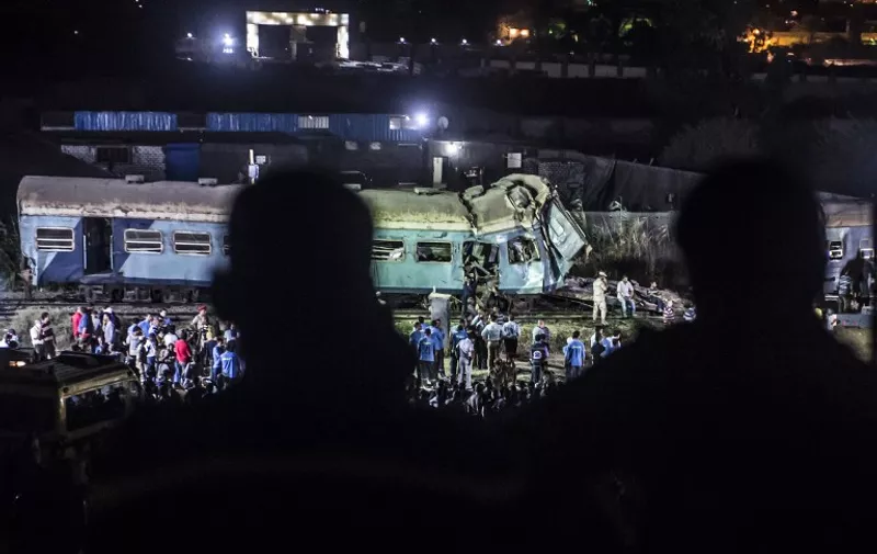 Local people look on as emergency personnel and officials remove the wreckage following a collision by two trains on August 11, 2017 near Khorshid station in Alexandria. 
At least 36 people were killed as two trains collided August 11 outside the Mediterranean city of Alexandria, in one of the deadliest in a string of such accidents in Egypt, the health ministry said. The crash also injured 123 people, the ministry said in a statement.
 / AFP PHOTO / KHALED DESOUKI