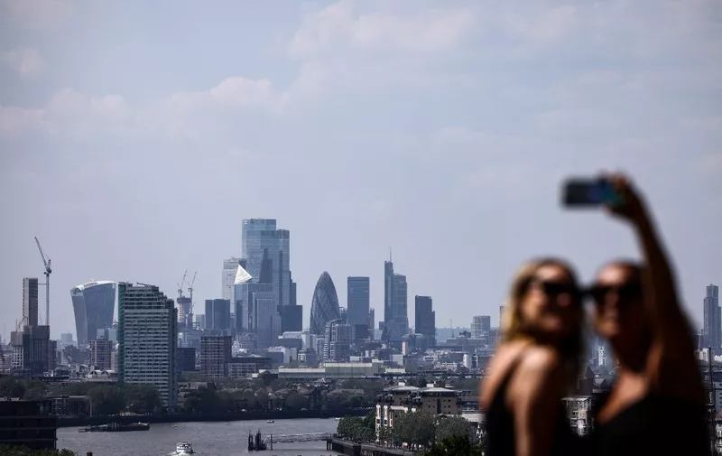 People take a selfie picture with the City financial district from a view point in Greenwich Park, in south east London on June 14, 2023. A high air pollution alert for the city of London has been extended to June 14, 2023 by the London City Hall, after it said local emissions had combined with warm weather. (Photo by HENRY NICHOLLS / AFP)