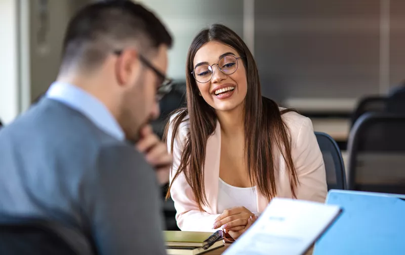 Portrait of young  female client or candidate sitting at table, talking to male manager and smiling in office. Job interview or consultancy concept. Young attractive woman during job interview