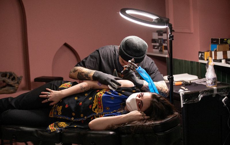 A tattooist works on a customer at the Heartbreak Social Club tatoo parlour in Dublin on December 1, 2020, as Ireland exits a second partial coronavirus lockdown. - Ireland ended a second partial coronavirus lockdown on Tuesday, with non-essential shops, hairdressers and gyms unlocking their doors after six weeks of tough restrictions. Museums, galleries, libraries, cinemas and places of worship also reopened as the nation lifted virus curbs in place since October 22. On Friday, pubs and restaurants serving food will follow suit, although drinking-only establishments will remain shuttered. (Photo by PAUL FAITH / AFP)