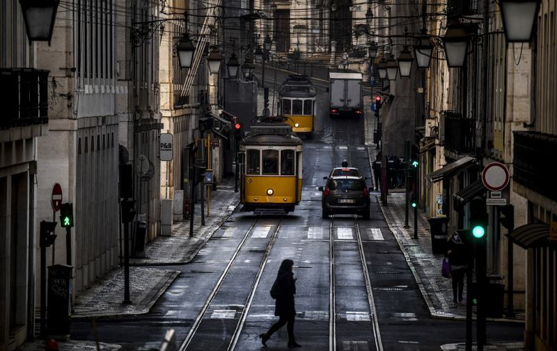 A woman crosses a street past trams in Lisbon on January 15, 2021 as Portugal entered a fresh lockdown over a surge in coronavirus cases. - The novel coronavirus has killed at least 1,994,833 people since the outbreak emerged in China in December 2019, according to a tally from official sources compiled by AFP. (Photo by PATRICIA DE MELO MOREIRA / AFP)