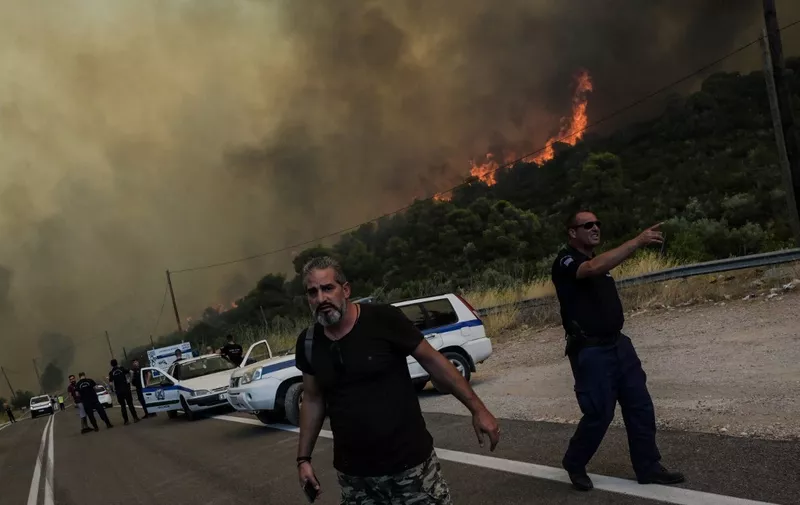 Police officers evacuate people as a wildfire burns, in the village of Agios Charalampos, near Athens, on July 18, 2023. Europe braced for new high temperatures on July 18, 2023, under a relentless heatwave and wildfires that have scorched swathes of the Northern Hemisphere, forcing the evacuation of 1,200 children close to a Greek seaside resort. Health authorities have sounded alarms from North America to Europe and Asia, urging people to stay hydrated and shelter from the burning sun, in a stark reminder of the effects of global warming. (Photo by Aris MESSINIS / AFP)
