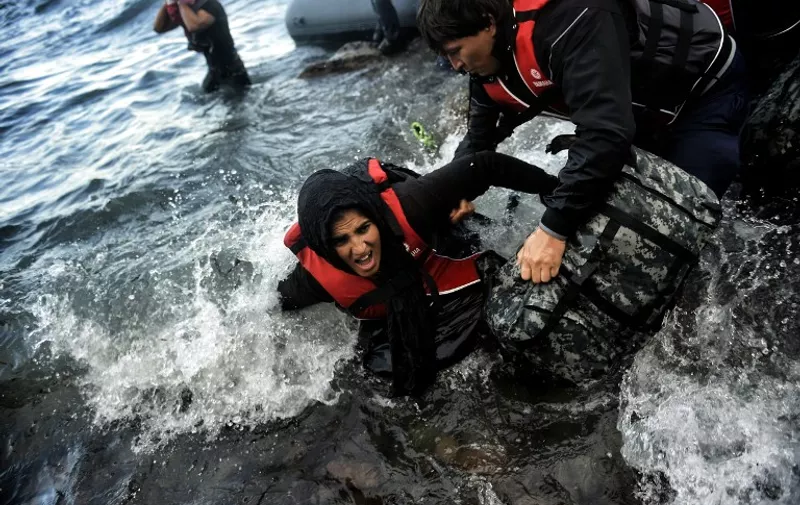 A woman is helped to her feet as refugees and migrants arrive at the Greek island of Lesbos after crossing the Aegean sea from Turkey on October 2, 2015. Greece's prime minister told the United Nations on October 1, that Athens was doing all it could to help the refugee and migrant crisis, and criticized the building of walls to keep them out. Around 330,000 people, most of them Syrians, Iraqis and Afghans fleeing war, have arrived on Greek shores so far this year, with another 3,000 still arriving every day, UN figures show. AFP PHOTO / ARIS MESSINIS