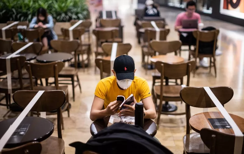 Customers sit in a cafe where social distancing between patrons has been enforced by placing white tape over unavailable tables and chairs as a precautionary measure against the COVID-19 coronavirus, in Hong Kong on March 31, 2020. (Photo by Anthony WALLACE / AFP)