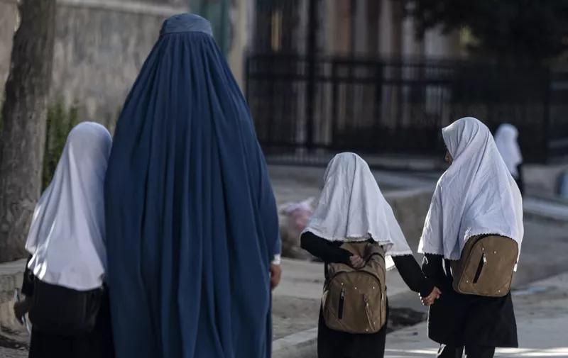In this picture taken on August 9, 2022, an Afghan woman walks with schoolgirls going to their primary school in Kabul. - One year on from the Taliban's return to power in Afghanistan, some cracks are opening within their ranks over the crucial question of just how much reform their leaders can tolerate. Infamous during their first reign for their brutal crackdowns on rights and freedoms, the Islamists vowed to rule differently this time. (Photo by Wakil KOHSAR / AFP) / TO GO WITH 'Afghanistan-Taliban-OneYear-Kandahar' FOCUS