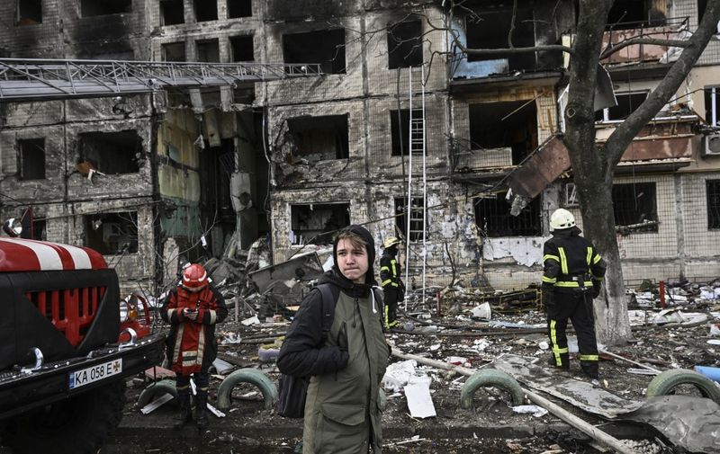 Maksim Korobych, 18-years-old, stands near firefighters in front of a destroyed apartment building after it was shelled in the northwestern Obolon district of Kyiv on March 14, 2022. - Two people were killed on March 14, 2022, as various neighbourhoods of the Ukraine capital Kyiv came under shelling and missile attacks, city officials said, on day 19 after the Russia's military invaded the Ukraine on February 24, 2022. (Photo by Aris Messinis / AFP)