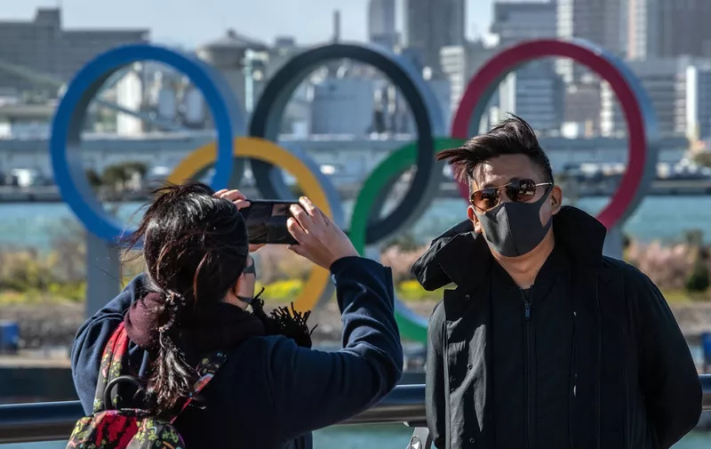TOKYO, JAPAN - MARCH 05: A man wearing a face mask has his photograph taken in front of the Olympic Rings in Odaiba on March 5, 2020 in Tokyo, Japan. An increasing number of events and sporting fixtures are being cancelled or postponed around Japan while some businesses are closing or asking their employees or work from home as Covid-19 cases continue to grow and concerns mount over the possibility that the epidemic will force the postponement or even cancellation of the Tokyo Olympics. (Photo by Carl Court/Getty Images)