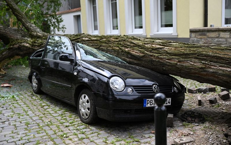 The trunk of a tree lies on a car in the city centre of Paderborn, western Germany on May 21, 2022, the day after a storm caused major damage. - Almost 40 people were injured, several seriously, on May 20 in a "tornado" which hit the western German city of Paderborn, the police and fire brigade said. A police spokesman said the tornado also caused significant damage in the city in the North Rhine-Westphalia state, following abnormally high temperatures for the time of year. (Photo by INA FASSBENDER / AFP)