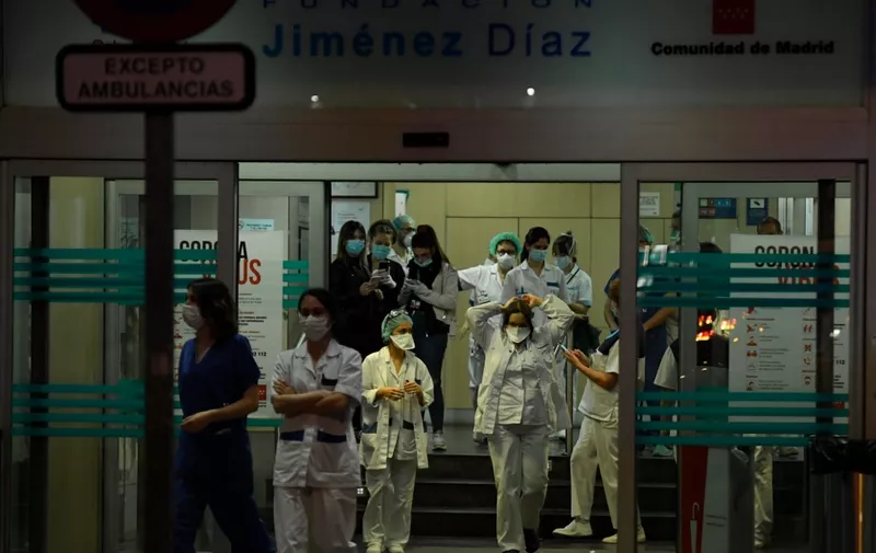 Healthcare workers dealing with the new coronavirus crisis stand at the entrance of the Fundacion Jimenez Diaz hospital in Madrid on March 25, 2020. - As the global death toll soared past 20,000, Spain joined Italy in seeing its number of fatalities overtake China, where the virus first emerged just three three months ago. (Photo by OSCAR DEL POZO / AFP)