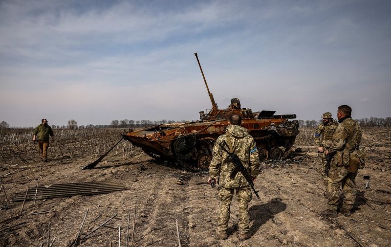 Ukrainian soldiers stand by a burnt Russian tank on the outskirts of Kyiv, on March 31, 2022, amid Russian invasion of Ukraine. (Photo by RONALDO SCHEMIDT / AFP)