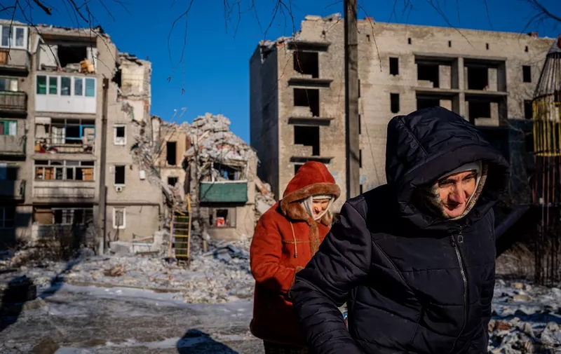 Elderly local residents walk past a destroyed residential building in Chasiv Yar, Eastern Ukraine, on January 7, 2023, amid the Russian invasion of Ukraine. - As artillery boomed outside and fighter jets flew overhead, Orthodox Christians in a battered east Ukraine town held a Christmas service in a basement shelter on January 7, vowing not to let war ruin the holiday. (Photo by Dimitar DILKOFF / AFP)