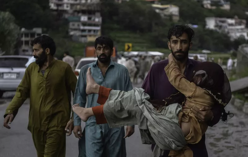 A man (R) carries his sick daughter along a road damaged by flood waters following heavy monsoon rains in Madian area in Pakistan's northern Swat Valley on August 27, 2022. - Thousands of people living near flood-swollen rivers in Pakistan's north were ordered to evacuate on August 27 as the death toll from devastating monsoon rains neared 1,000 with no end in sight. (Photo by Abdul MAJEED / AFP)