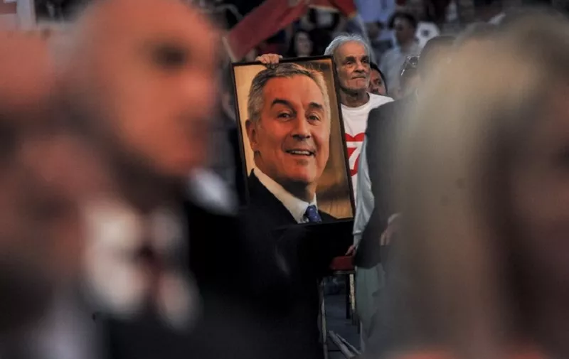 A supporter holds a picture of the presidential candidate of the ruling Democratic party of Socialist Milo Djukanovic during a pre-election rally in Podgorica on April 12, 2018. 
Gangland killings and organised crime have loomed over Montenegro's presidential campaign, handing ammunition to the opposition in their attacks on six-time former prime minister Milo Djukanovic, who is the favourite to win April 15, first round vote. / AFP PHOTO / SAVO PRELEVIC