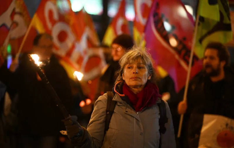 A demonstrator holds a torchlight during a procession against a pension reform in Paris, on January 26, 2023. - France's government on January 23, 2023, moved forward with a fiercely contested pensions reform plan that would raise the retirement age to 64, saying balancing the system's books must be top priority. (Photo by Emmanuel DUNAND / AFP)