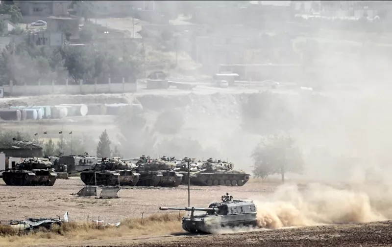 Vehicles of the Turkish army move on a dirt road as the city of Kobane is pictured in the background on June 26, 2015 in Suruc, Turkey. Hundreds of Syrians from the region of Kobane were waiting at the fence on the Syria-Turkey border as clashes continued between Kurdish fighters and Islamist jihadists, an AFP photographer reported. Mainly Kurdish Kobane had been re-captured by Kurdish fighters from Islamic State (IS) jihadists in January and some residents had then cautiously returned to the town from their refuge in Turkey. AFP PHOTO / BULENT KILIC