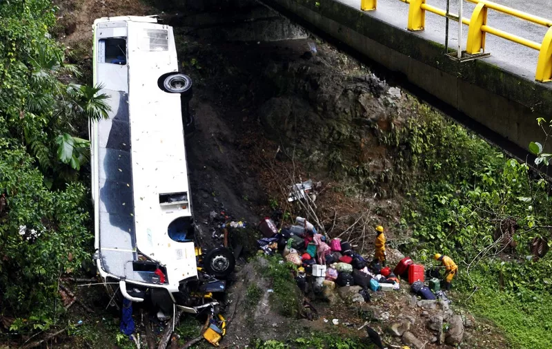 Rescue workers recover belonging of passengers from the wreckage of a bus that plunged down the road connecting Medellin and Bogota, near San Luis, on December 27, 2021. Seven people, including a pregnant woman, died and 20 were injured when a bus plunged into a ravine in Antioquia Province. (Photo by FREDY BUILES / AFP)