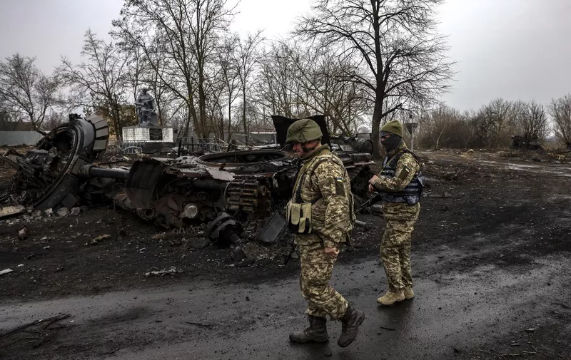 Ukrainian soldiers patrol next to a destroyed Russian tank in the village of Lukianivka near Kyiv on March 30, 2022. (Photo by RONALDO SCHEMIDT / AFP)