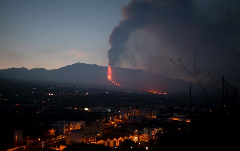 Buildings and housing are pictured as the Cumbre Vieja volcano in the background spews lava, ash and smoke, in Los Llanos de Aridane, in the Canary Island of La Palma on October 4, 2021. - A new flow of highly liquid lava emerged from the volcano erupting in Spain's Canary islands on October 1, authorities said, as a huge magma shelf continues to build on the Atlantic ocean. (Photo by JORGE GUERRERO / AFP)