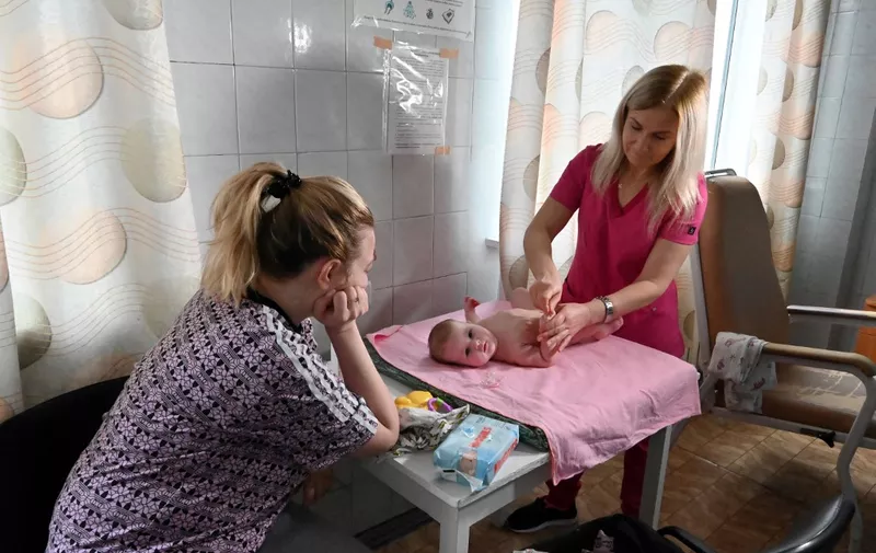 A nurse teaches a mother how to massage her newborn baby in a room at the Kharkiv City Perinatal Center which did not stop working even after the Russian invasion of Ukraine, in Kharkiv on December 12, 2022. (Photo by SERGEY BOBOK / AFP)