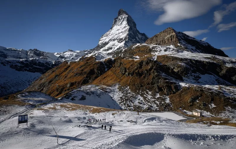 Tourists stand on the snow next to the Matterhorn mountain above the resort of Zermatt in the Swiss Alps on November 28, 2020. (Photo by Fabrice COFFRINI / AFP)