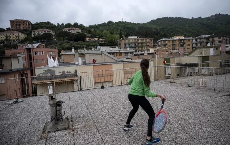 Vittoria Oliveri (front) plays tennis with Carola in background on rooftops of their house in Finale Ligure, Liguria Region, northwestern Italy on April 19, 2020, during the country's lockdown aimed at stopping the spread of the COVID-19 (new coronavirus) pandemic. - Everyday Carola, 11, and Vittoria, 13, play tennis from a rooftop to another rooftop of their homes to practice during the Covid 19 lockdown. (Photo by MARCO BERTORELLO / AFP)