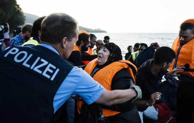 A German police officer, representative of the EU's border management agency Frontex, helps refugees and migrants arriving on the Greek island of Lesbos after crossing the Aegean Sea from Turkey, on October 17, 2015. Twelve migrants drowned when their boat sank off the Turkish coast as they were seeking to reach Greece, while around 25 others were rescued, the Anatolia news agency reported.   AFP PHOTO / DIMITAR DILKOFF