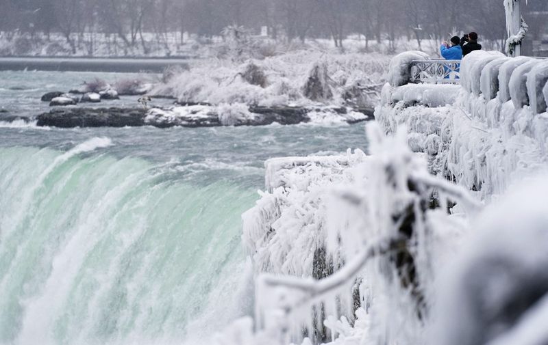 Two men take photographs at the Horseshoe Falls in Niagara Falls, Ontario, on January 27, 2021. (Photo by Geoff Robins / AFP)