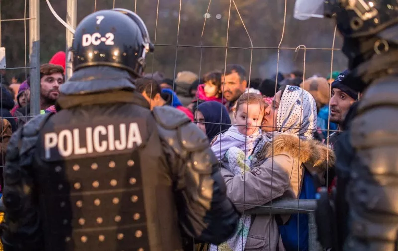 Slovenian riot policemen stand by a fence as a crowd of migrants and refugees wait to cross the Slovenian-Austrian border in Sentilj, Slovenia, to Spielfeld, Austria, on October 29, 2015. Austria on October 28  announced plans to build a fence at a major border crossing with fellow EU state Slovenia to "control" the migrant influx, in a blow to the bloc's cherished passport-free Schengen zone. AFP PHOTO / RENE GOMOLJ