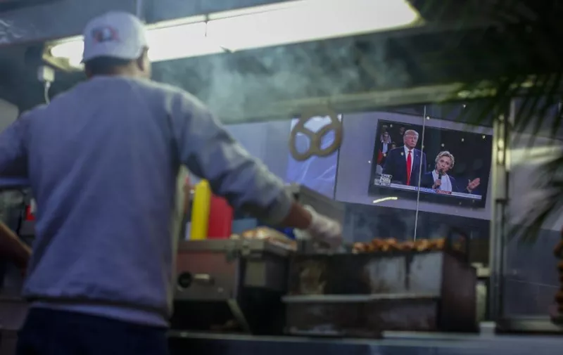 The second presidential debate between US Democratic presidential candidate Hillary Clinton and US Republican presidential candidate Donald Trump is seen on a screen as a man sells food in Times Square in New York on October 9, 2016.  / AFP PHOTO / KENA BETANCUR