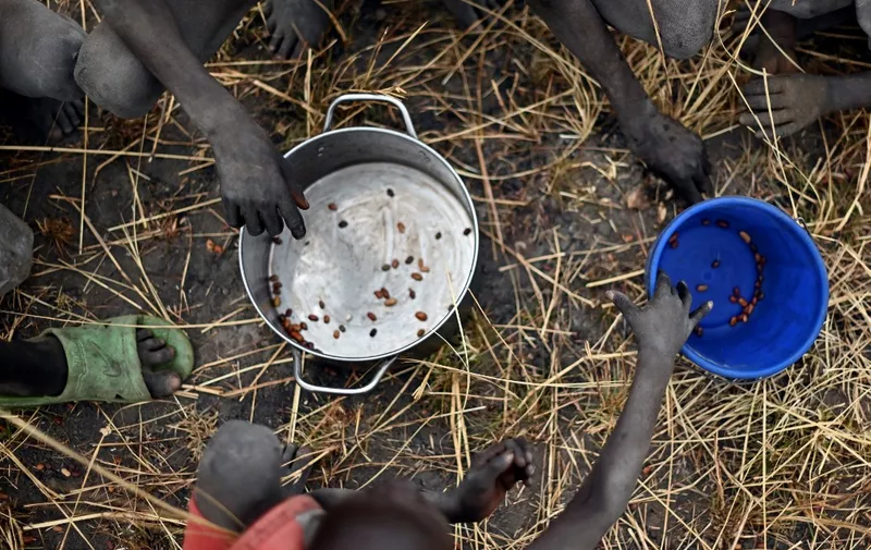 Children collect grain spilt on the field from gunny bags that ruptured upon ground impact following a food drop from a plane at a village in Ayod county, South Sudan, where World Food Programme (WFP) have just carried out a food drop of grain and supplementary aid on February 6, 2020. The villagers hear the distant roar of jet engines before a cargo plane makes a deafening pass over Mogok, dropping sacks of grain from its hold to the marooned dust bowl below. South Sudan is the last place on earth where food is airdropped, and in Mogok there was little other choice: without the tonnes of grains and cereals, people would have simply perished. (Photo by TONY KARUMBA / AFP)