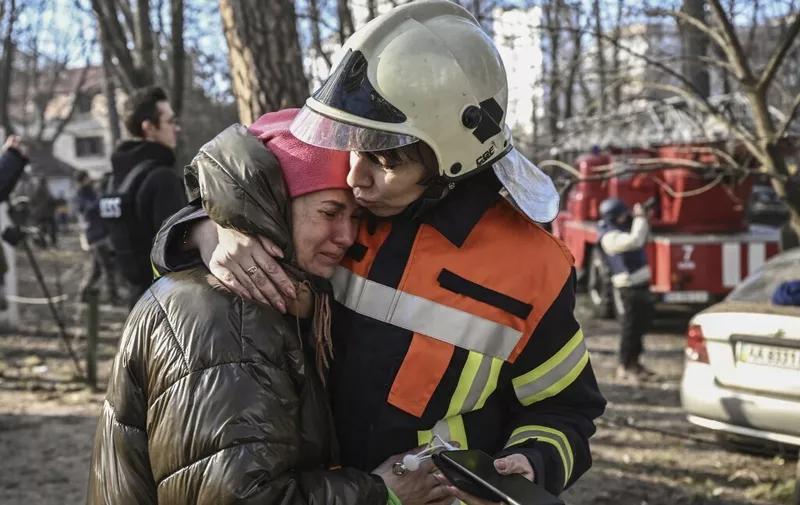 An evacuated resident is comforted by a rescue staff outside a burning apartment building in Kyiv on March 15, 2022, after strikes on residential areas killed at least two people, Ukraine emergency services said as Russian troops intensified their attacks on the Ukrainian capital. - A series of powerful explosions rocked residential districts of Kyiv early today killing two people, just hours before talks between Ukraine and Russia were set to resume. (Photo by Aris Messinis / AFP)