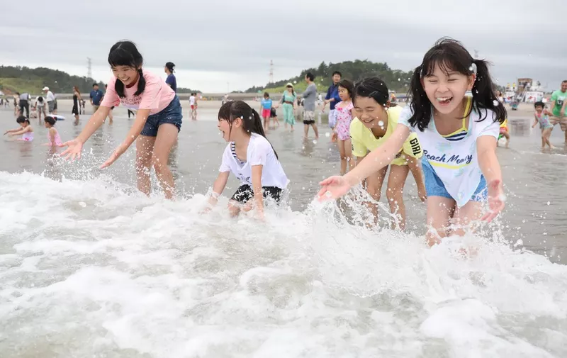Children play with waves during the opening of the beach to members of the public at Kita Izumi in Minami Soma city, Fukushima prefecture on July 20, 2019. - The beach was closed for more than eight years following the Fukushima Daiichi nuclear power plant accident in 2011. (Photo by JIJI PRESS / JIJI PRESS / AFP) / Japan OUT