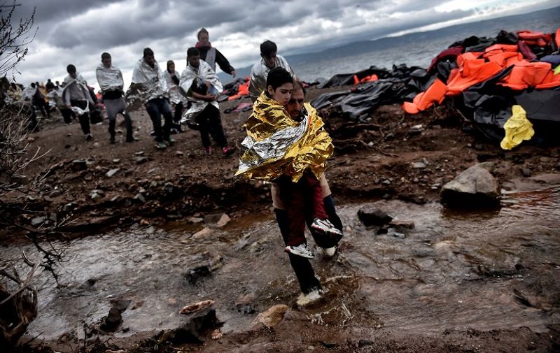 Refugees and migrants wearing emergency blankets to warm themselves, walk on the beach as they just arrived on the Greek island of Lesbos, after crossing the Aegean sea from Turkey on October 24, 2015. Bulgaria, Romania and Serbia on October 24 threatened to close their borders if EU countries stopped accepting migrants, as European leaders prepared for a mini summit on the continent's worst refugee crisis since World War II. AFP PHOTO / ARIS MESSINIS